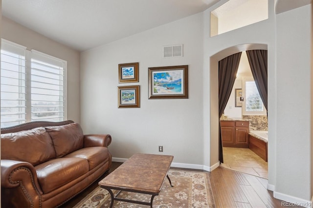 living room with visible vents, arched walkways, light wood finished floors, baseboards, and vaulted ceiling