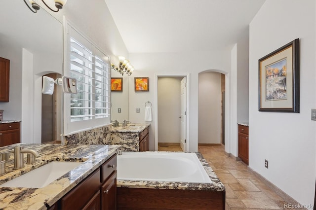 bathroom featuring stone tile floors, two vanities, a bath, and a sink