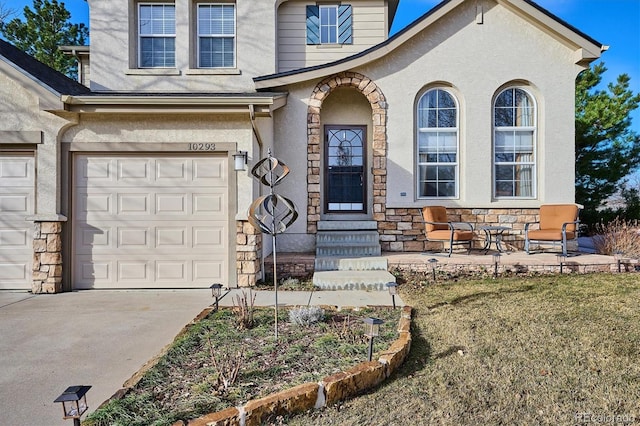 doorway to property with stucco siding, stone siding, an attached garage, and driveway