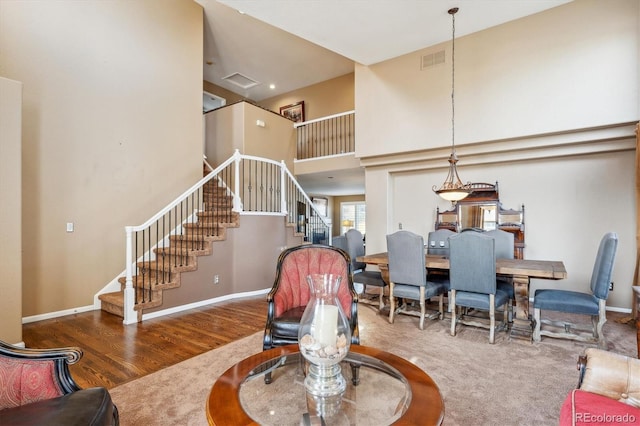 living area with stairway, wood finished floors, baseboards, visible vents, and a high ceiling