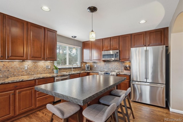 kitchen with light wood finished floors, a sink, appliances with stainless steel finishes, a kitchen bar, and tasteful backsplash