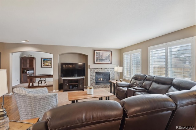 living area featuring arched walkways, a fireplace, baseboards, and wood finished floors