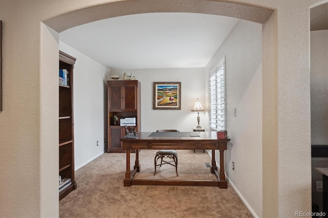 carpeted office space featuring baseboards, arched walkways, and a textured wall