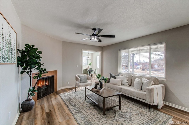 living room featuring ceiling fan, hardwood / wood-style floors, a tile fireplace, and a textured ceiling