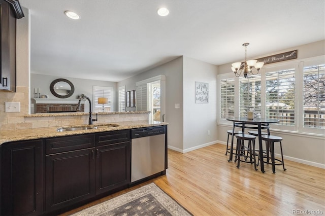 kitchen featuring light stone countertops, sink, tasteful backsplash, stainless steel dishwasher, and a chandelier