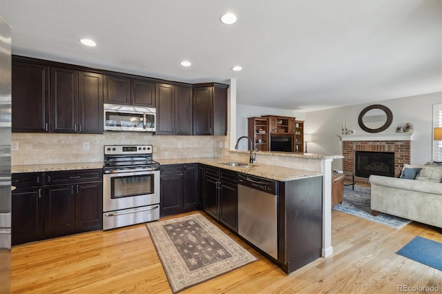 kitchen with sink, a brick fireplace, light hardwood / wood-style flooring, kitchen peninsula, and appliances with stainless steel finishes