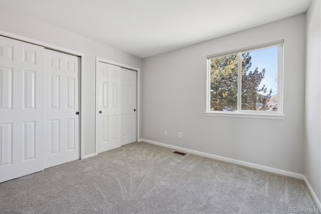 unfurnished bedroom featuring light carpet and two closets