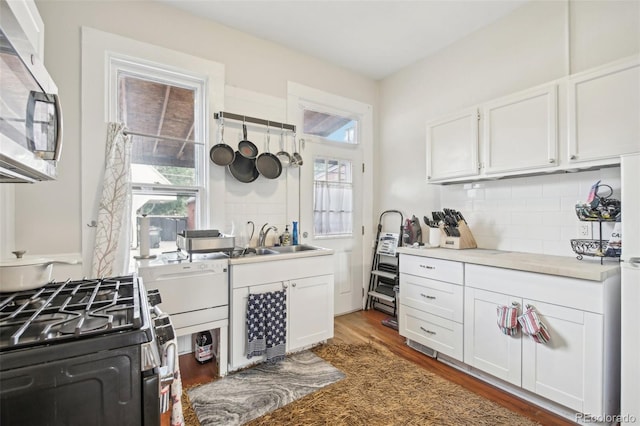 kitchen with white cabinetry, gas range oven, backsplash, hardwood / wood-style flooring, and sink