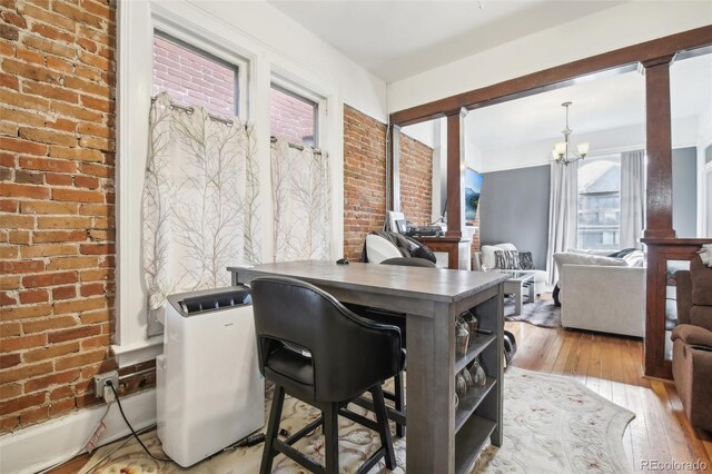 home office with a chandelier, decorative columns, brick wall, and light wood-type flooring