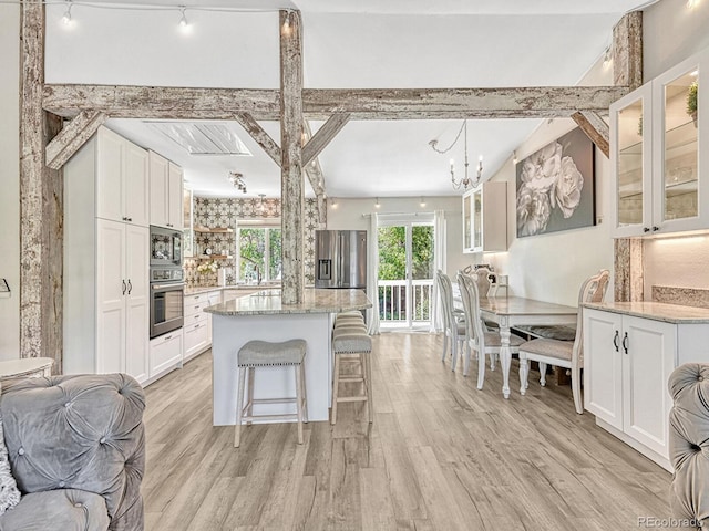 kitchen featuring light stone countertops, light wood-type flooring, stainless steel appliances, decorative light fixtures, and white cabinets