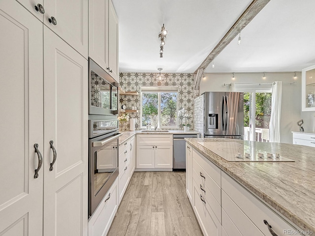 kitchen with light stone countertops, stainless steel appliances, white cabinetry, and a healthy amount of sunlight