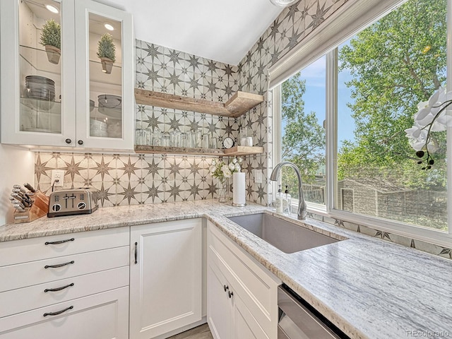 kitchen with white cabinets, light stone counters, a wealth of natural light, and sink