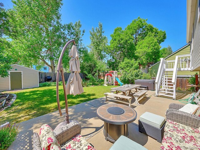 view of patio / terrace with a playground, an outdoor living space with a fire pit, a hot tub, and a storage shed