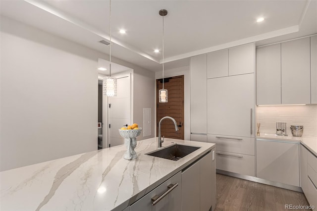 kitchen with tasteful backsplash, light stone counters, dark hardwood / wood-style flooring, pendant lighting, and sink