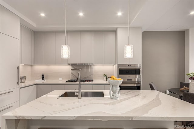 kitchen featuring pendant lighting, light stone countertops, a center island with sink, and stainless steel appliances