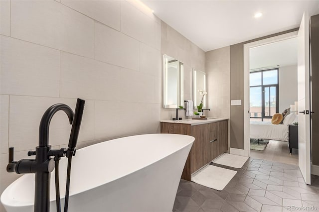 bathroom with tile walls, tile patterned flooring, a bath, and vanity