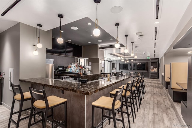 kitchen with a kitchen bar, light wood-type flooring, hanging light fixtures, and dark stone countertops