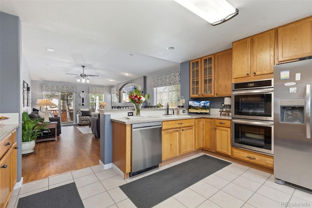 kitchen featuring a sink, a peninsula, open floor plan, glass insert cabinets, and stainless steel appliances