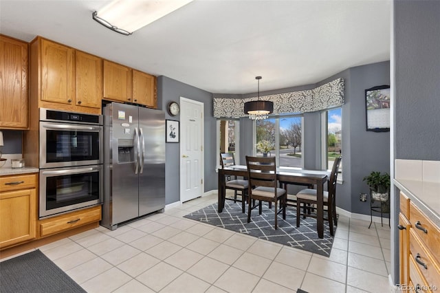 kitchen featuring light countertops, a chandelier, brown cabinets, appliances with stainless steel finishes, and light tile patterned floors
