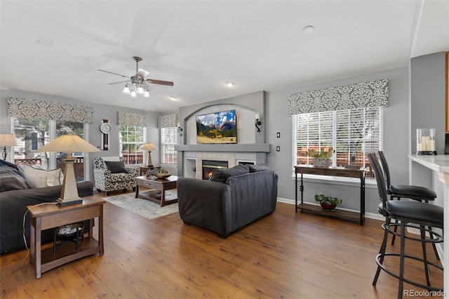 living area featuring a glass covered fireplace, baseboards, a ceiling fan, and wood finished floors