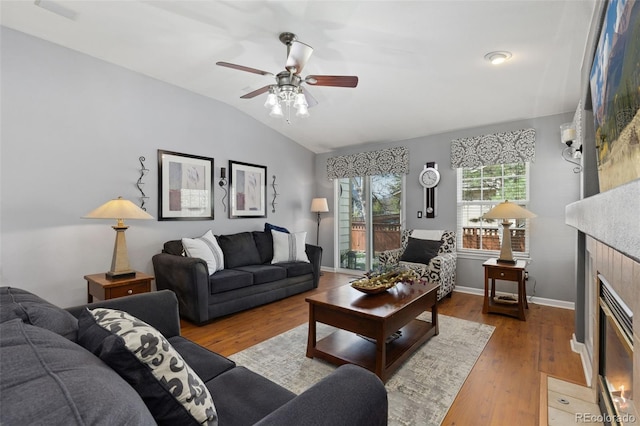 living room featuring ceiling fan, a fireplace, wood finished floors, baseboards, and lofted ceiling