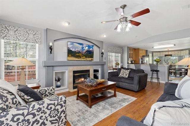 living area with ceiling fan, wood finished floors, vaulted ceiling, and a tile fireplace