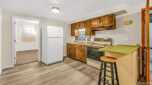 kitchen featuring light hardwood / wood-style floors, sink, kitchen peninsula, a kitchen breakfast bar, and white appliances