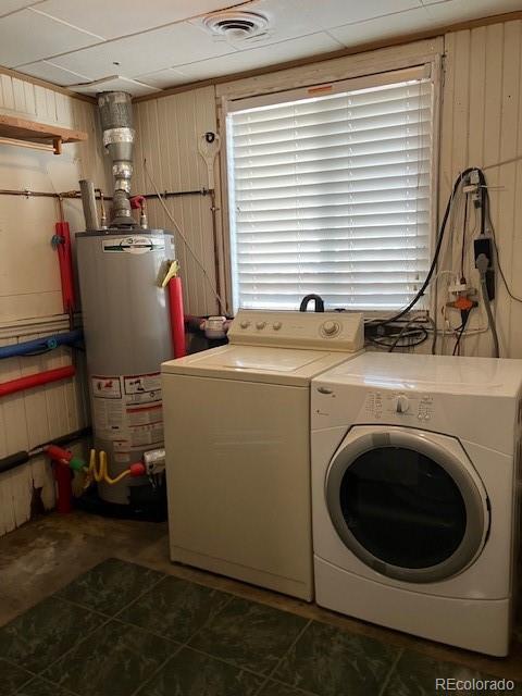 clothes washing area with washing machine and clothes dryer, water heater, and wood walls