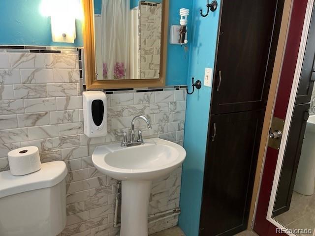 bathroom featuring tile walls, curtained shower, and toilet