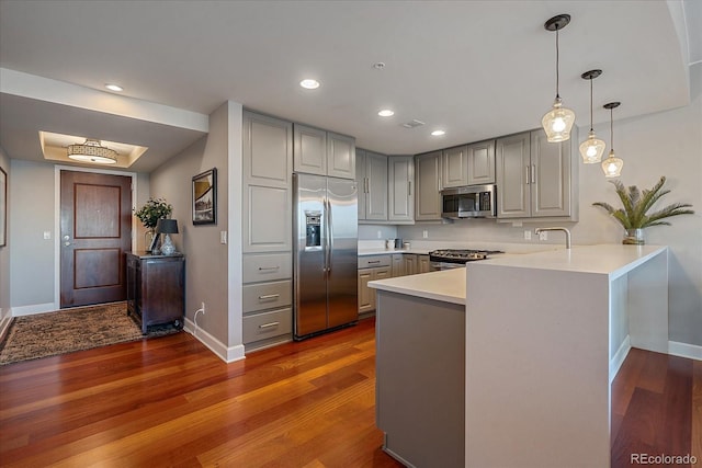 kitchen featuring kitchen peninsula, hardwood / wood-style floors, stainless steel appliances, and gray cabinetry