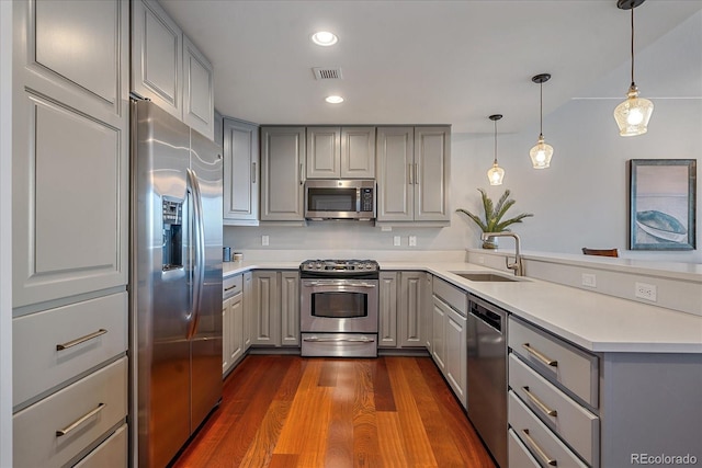 kitchen featuring gray cabinetry, dark wood-type flooring, sink, decorative light fixtures, and stainless steel appliances