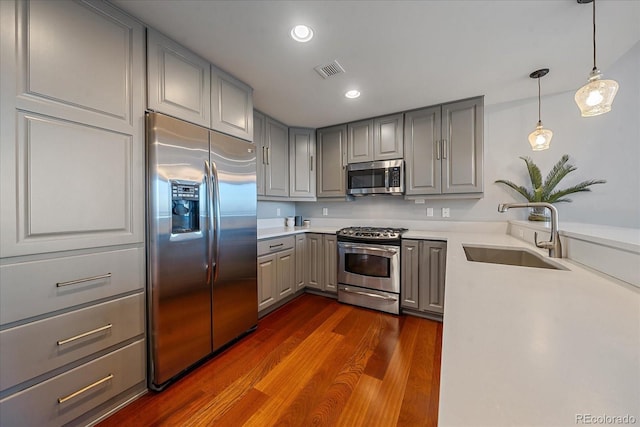 kitchen with sink, hanging light fixtures, dark hardwood / wood-style floors, gray cabinets, and appliances with stainless steel finishes