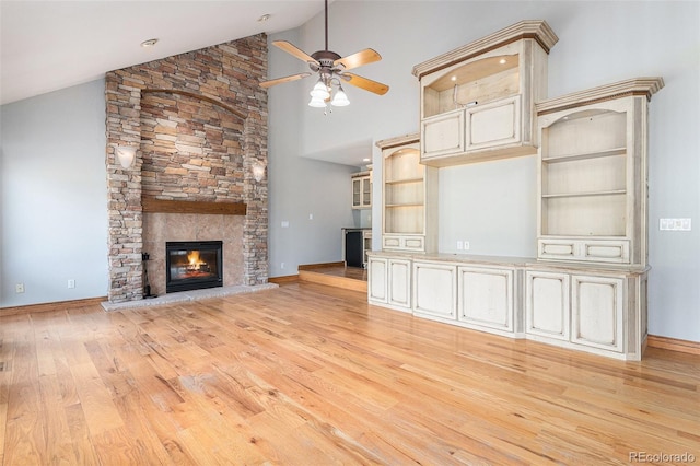 unfurnished living room featuring ceiling fan, light hardwood / wood-style floors, a stone fireplace, and high vaulted ceiling