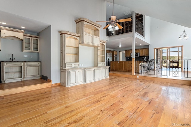 unfurnished living room with a high ceiling, ceiling fan with notable chandelier, and light hardwood / wood-style floors