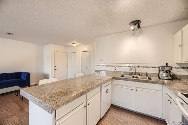 kitchen with sink, white cabinets, light wood-type flooring, and kitchen peninsula