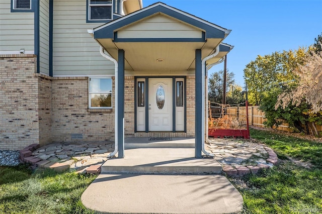 view of exterior entry with brick siding, crawl space, and fence