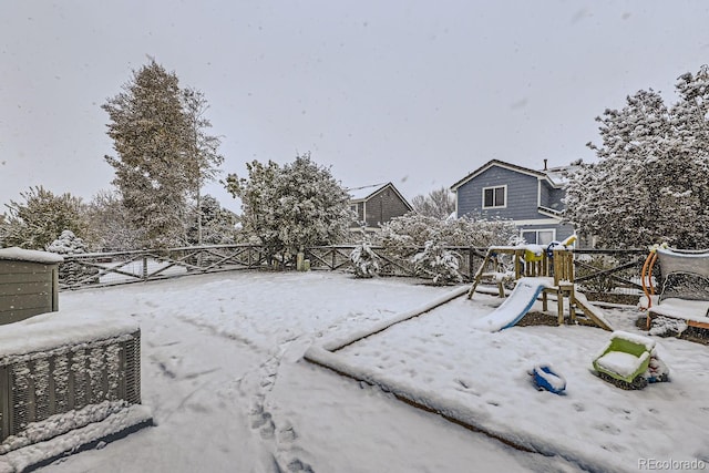 yard layered in snow featuring fence and a playground