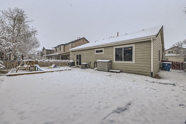 snow covered property with a playground, fence, and central AC