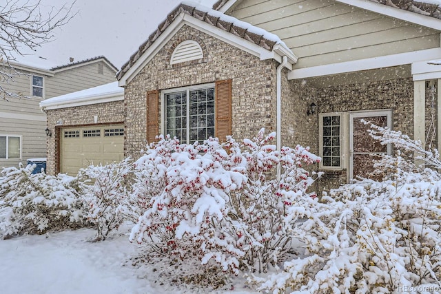 snow covered property with brick siding and an attached garage