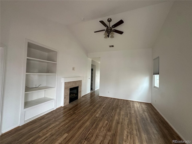 unfurnished living room with built in shelves, dark wood-style flooring, a ceiling fan, vaulted ceiling, and a tiled fireplace