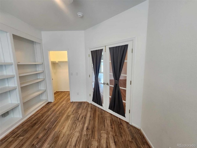 interior space with french doors, wood finished floors, a walk in closet, and baseboards