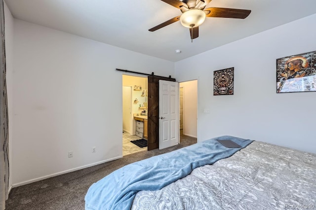 carpeted bedroom featuring ensuite bath, a barn door, baseboards, and a ceiling fan