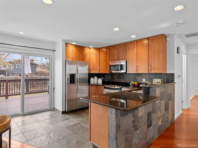 kitchen with dark stone counters, appliances with stainless steel finishes, a sink, backsplash, and recessed lighting