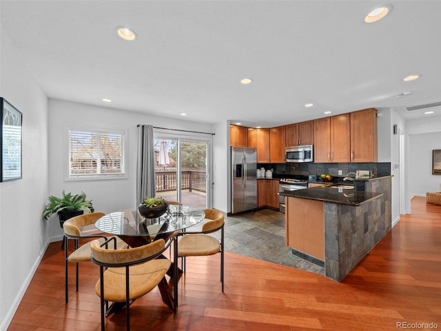 kitchen featuring stainless steel appliances, a peninsula, wood finished floors, a sink, and decorative backsplash