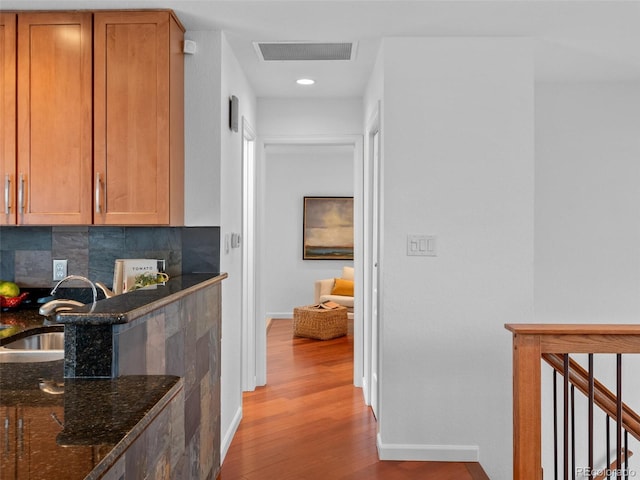 hallway with baseboards, visible vents, wood finished floors, an upstairs landing, and a sink