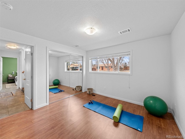 workout room with baseboards, a textured ceiling, visible vents, and wood finished floors