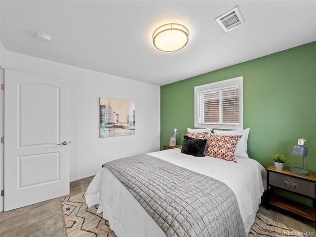 bedroom with a textured ceiling, light tile patterned floors, and visible vents