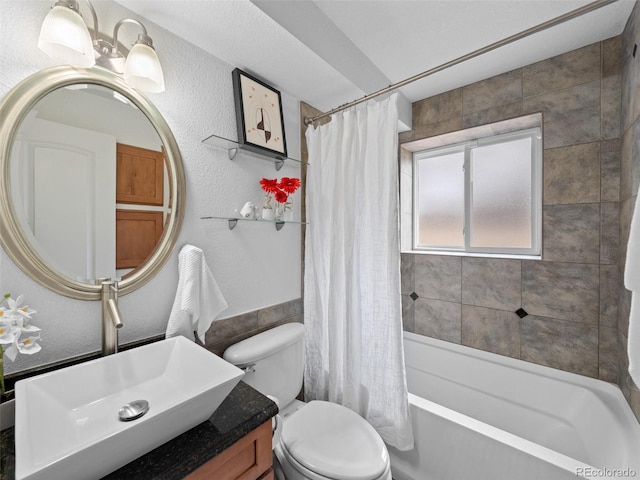 bathroom featuring toilet, a textured wall, shower / bath combination with curtain, and vanity