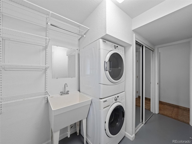 laundry area with stacked washer and dryer, a textured wall, a sink, and baseboards