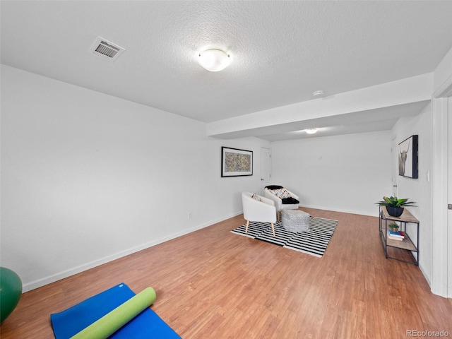 exercise room featuring a textured ceiling, wood finished floors, visible vents, and baseboards